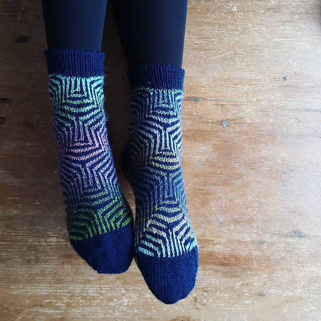 A pair of hand-knitted socks with a sort of geometric mosaic pattern of navy blue and rainbow shades.
