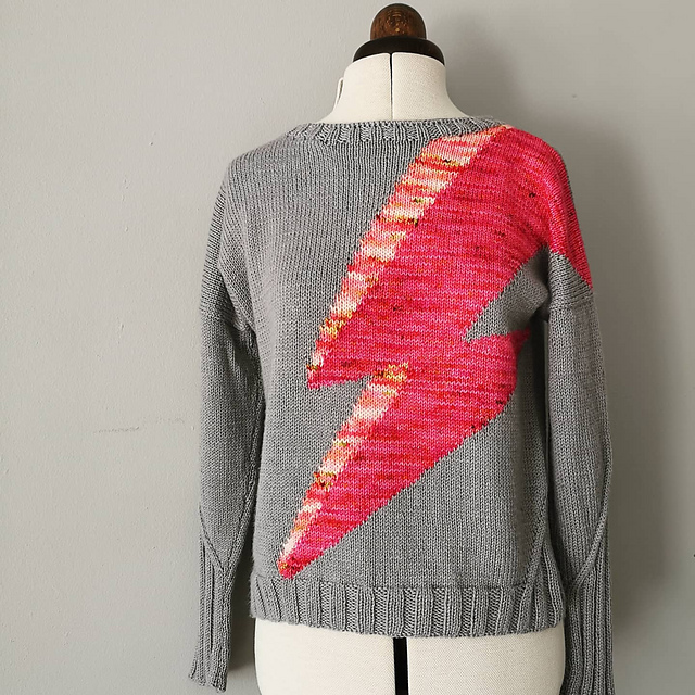 A hand-knitted jumper in pale grey yarn with a large, extremely bright pink lightning flash across the front